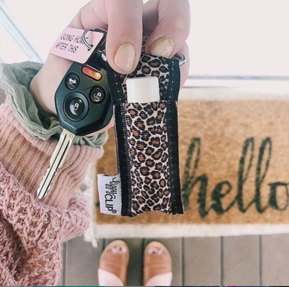 Hand holding a leopard print keychain with a key, wearing a pink sweater, on a 'hello' doormat.