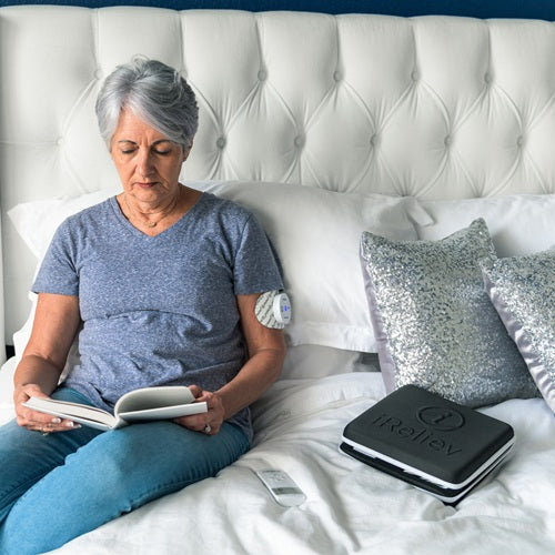 Hard carry case with iReliev devices on bed near a seated person holding controls