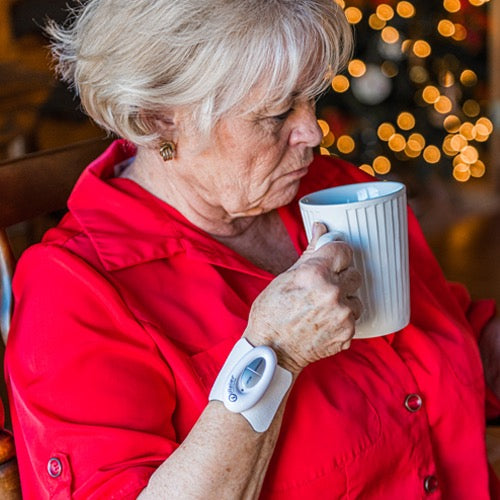 Mini pain relief patch controller applied to forearm while holding a mug