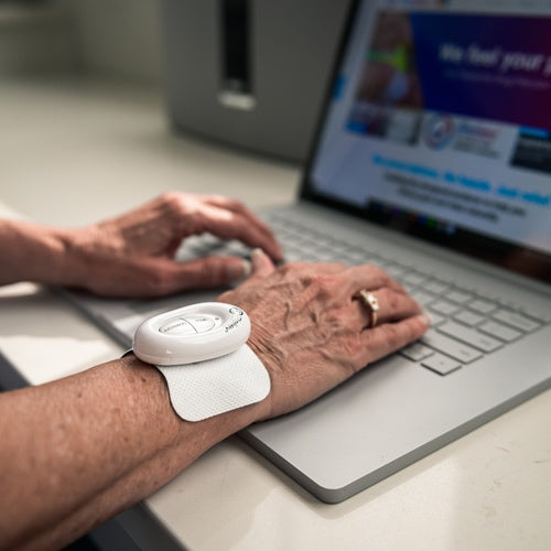 Mini pain relief controller and textured adhesive pad on forearm near a laptop