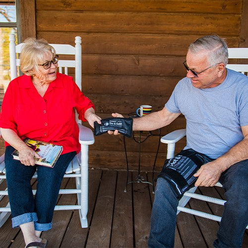 Two people each using black therapy gel packs on their laps while seated outside.