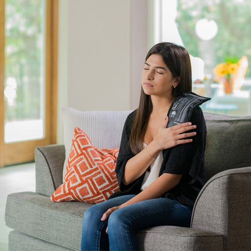 Hot and cold therapy gel pack worn on an arm over clothing while seated on a couch.