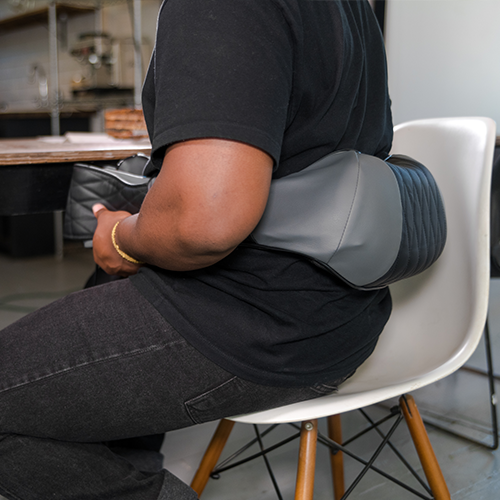 Neck and back massager strapped around an arm and upper back on a chair