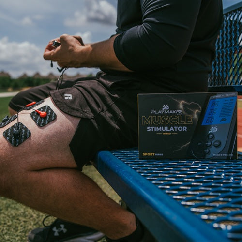 Muscle stimulator electrode pads on shorts-clad leg with controller and product box