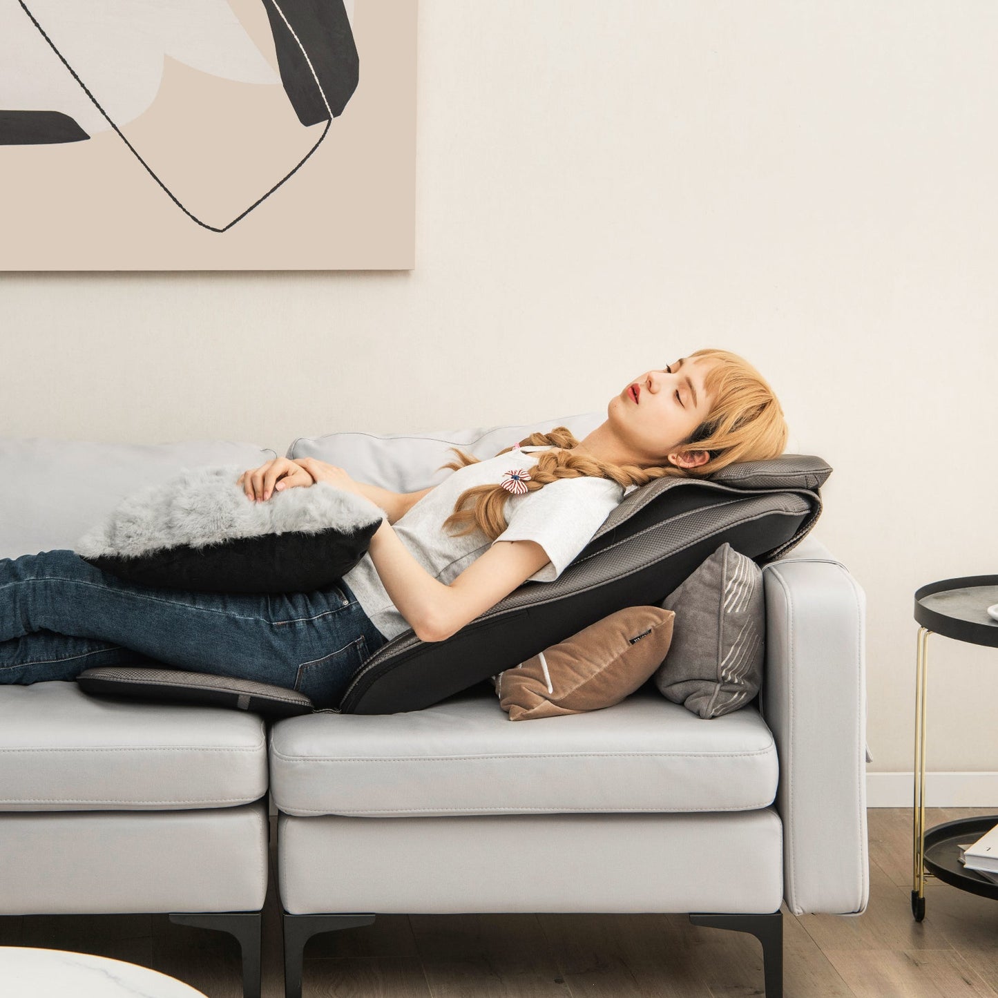 Woman relaxing on a sofa with a black massage chair pad with heat and vibration