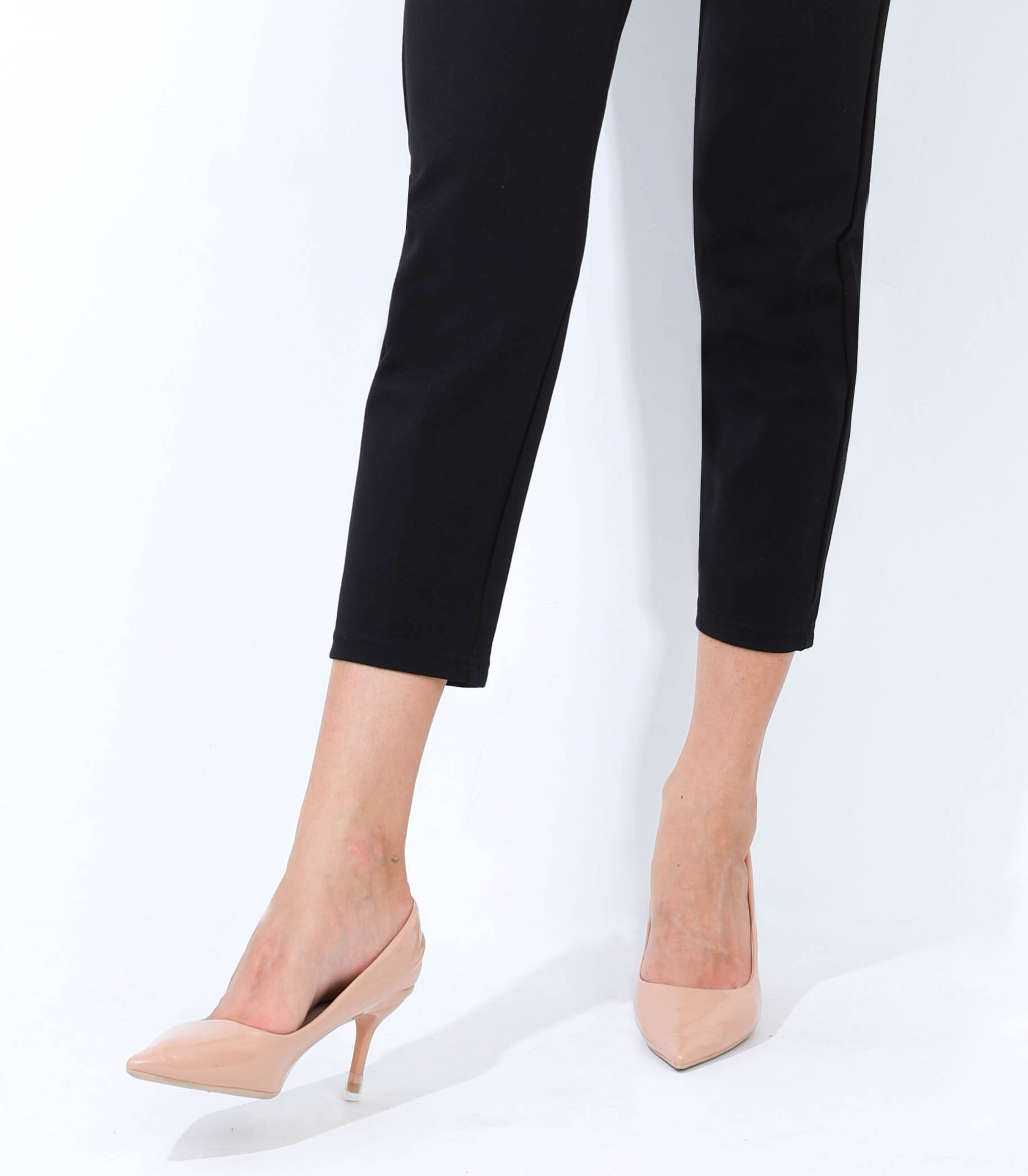 Person wearing black pants and beige high-heeled shoes on a white background