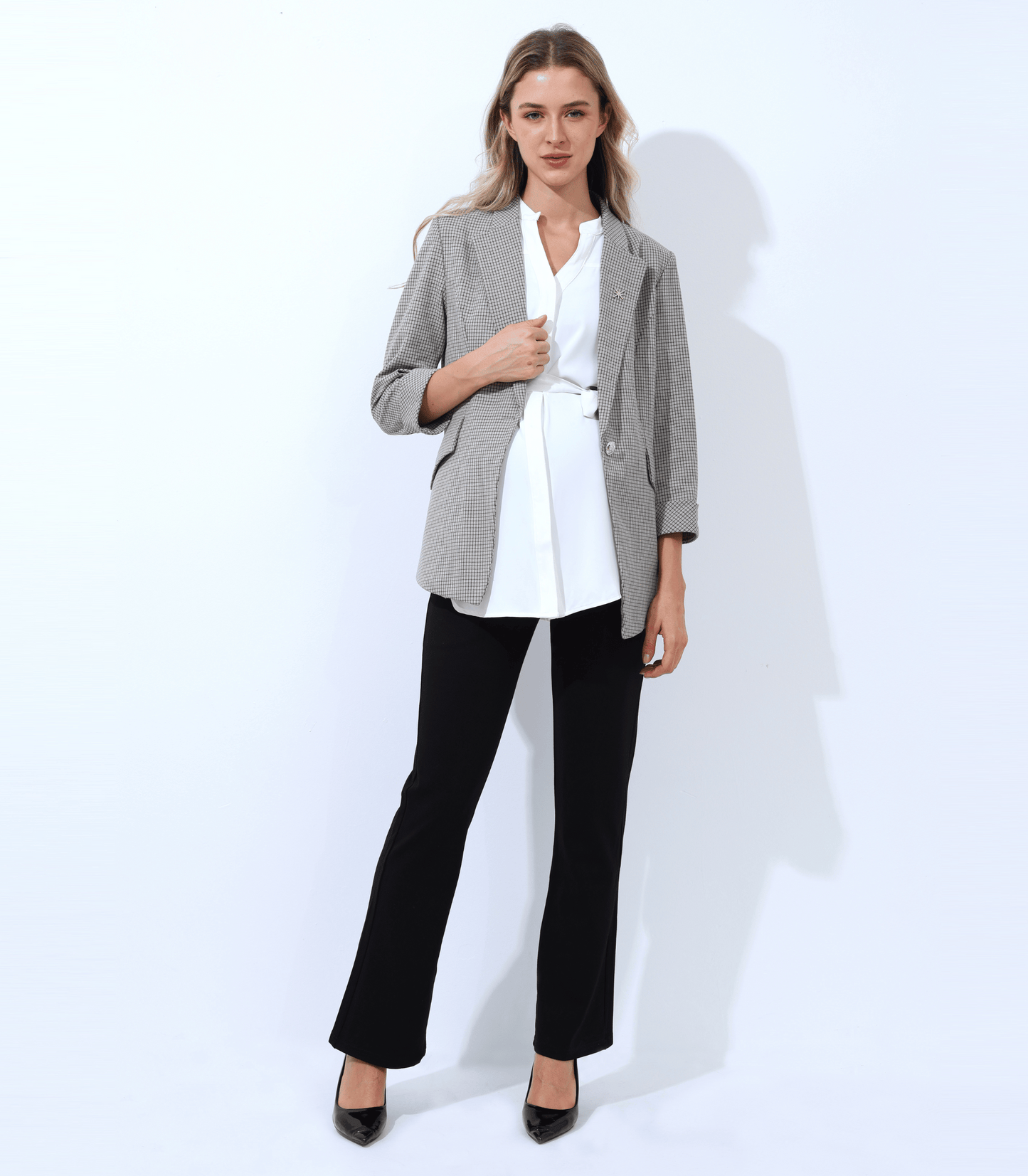 Woman wearing a gray blazer, white shirt, black pants, and black shoes on a white background