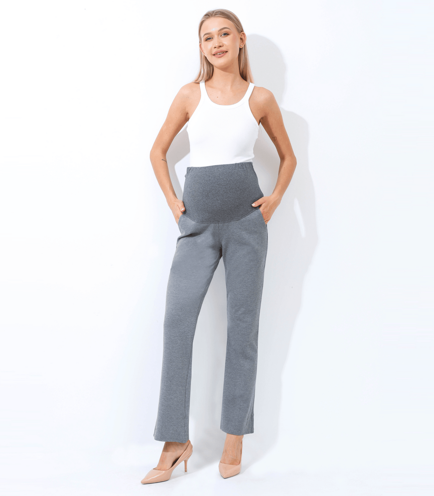 Woman wearing a white sleeveless top and gray high-waisted pants on a white background