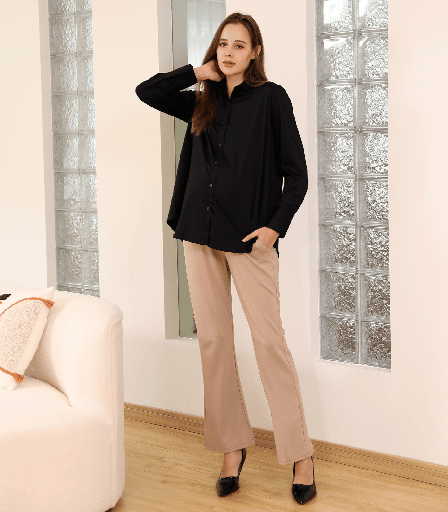 Woman wearing a black blouse and beige pants standing in a room with glass block walls.