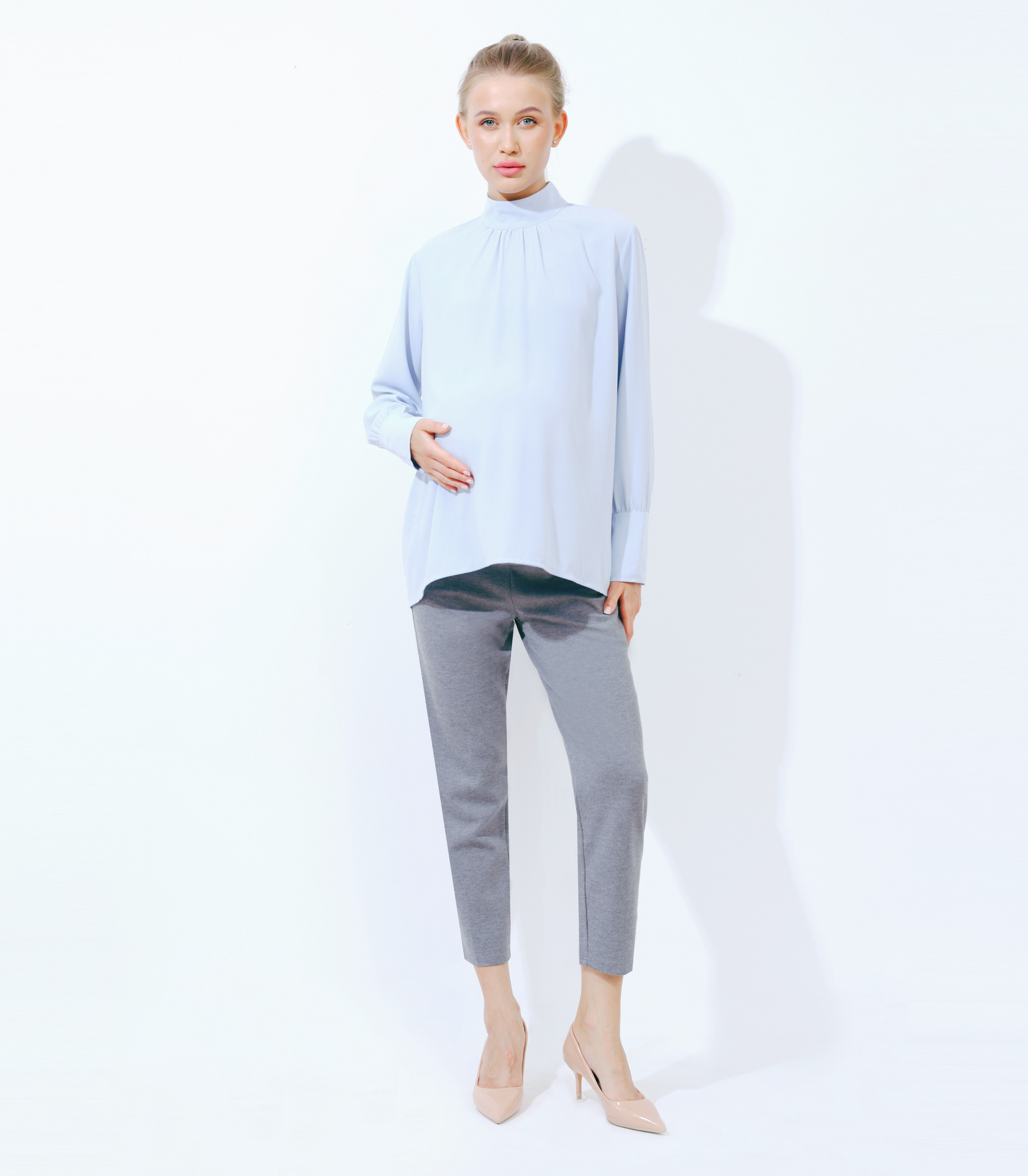 Woman wearing a light blue blouse and gray pants on a white background