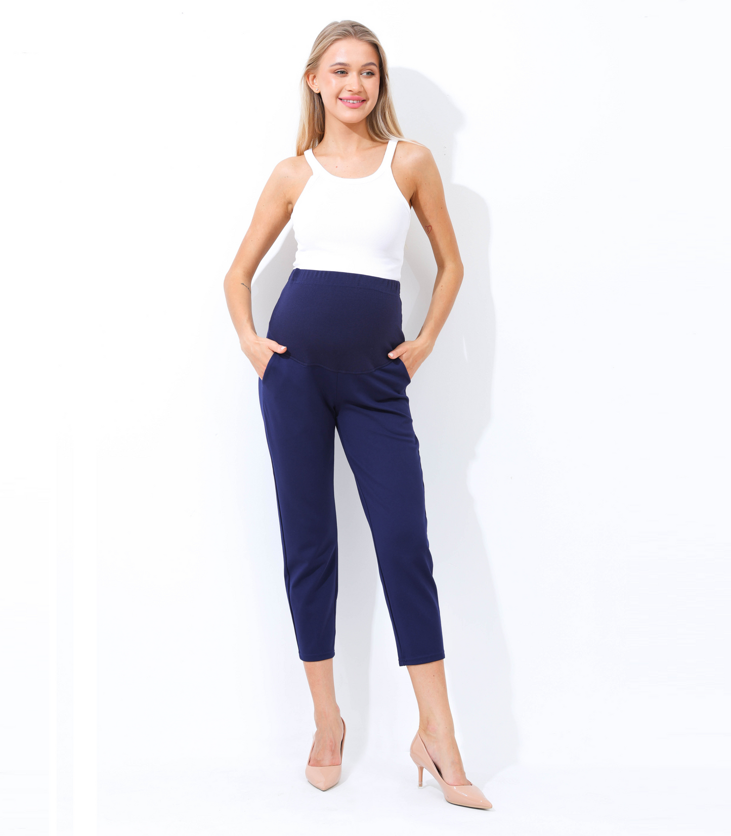 Woman wearing a white sleeveless top and navy blue pants on a white background