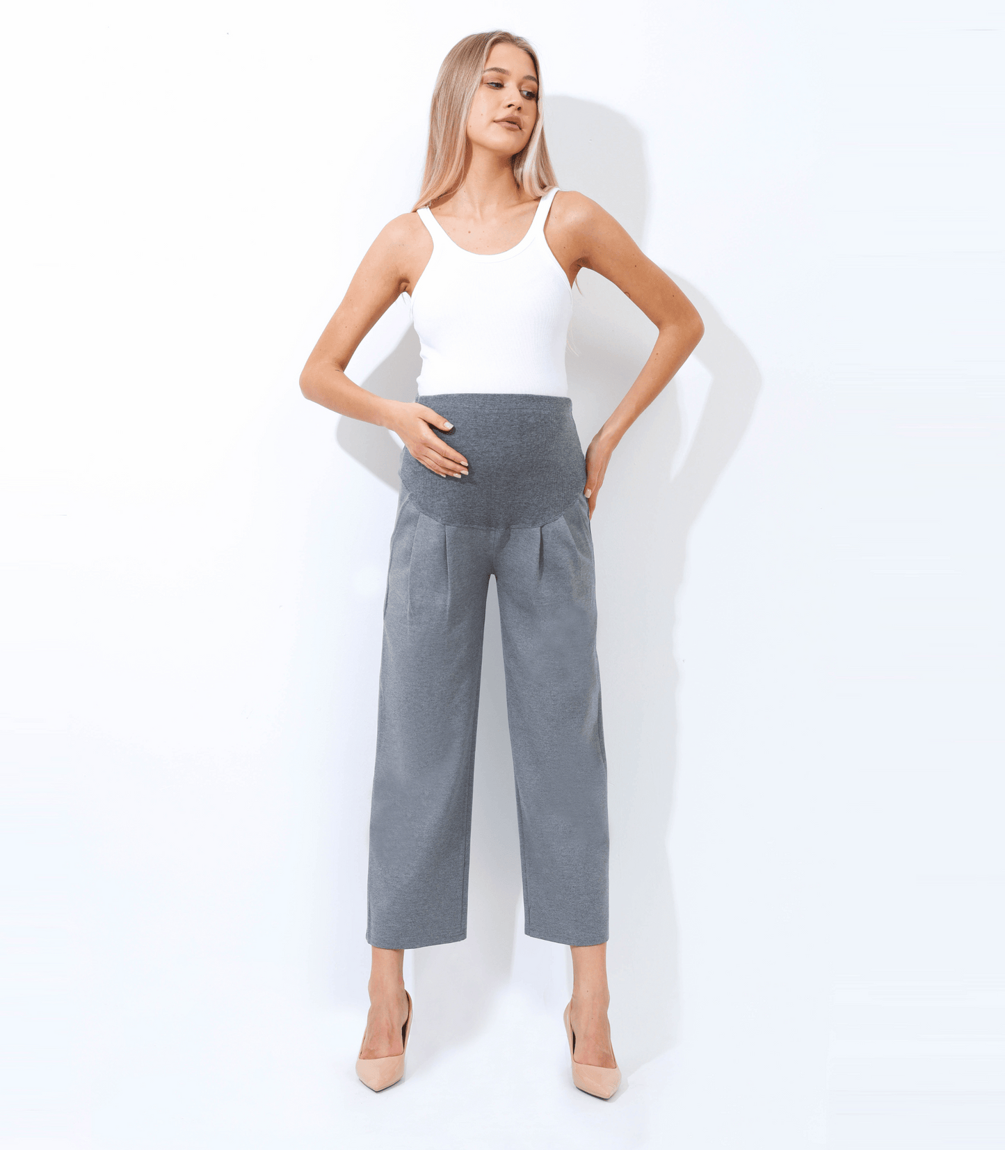 Woman wearing a white sleeveless top and gray high-waisted pants on a white background