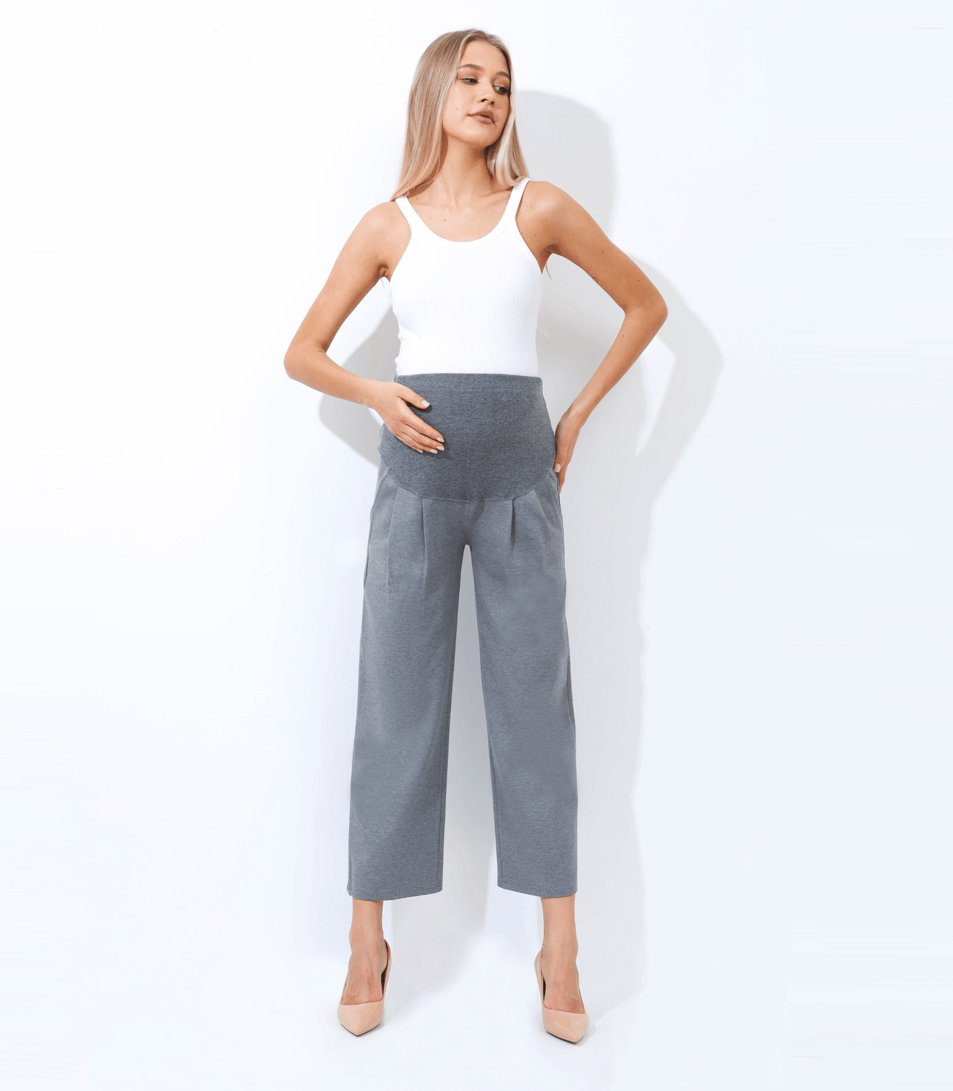 Woman wearing a white sleeveless top and gray high-waisted pants on a white background