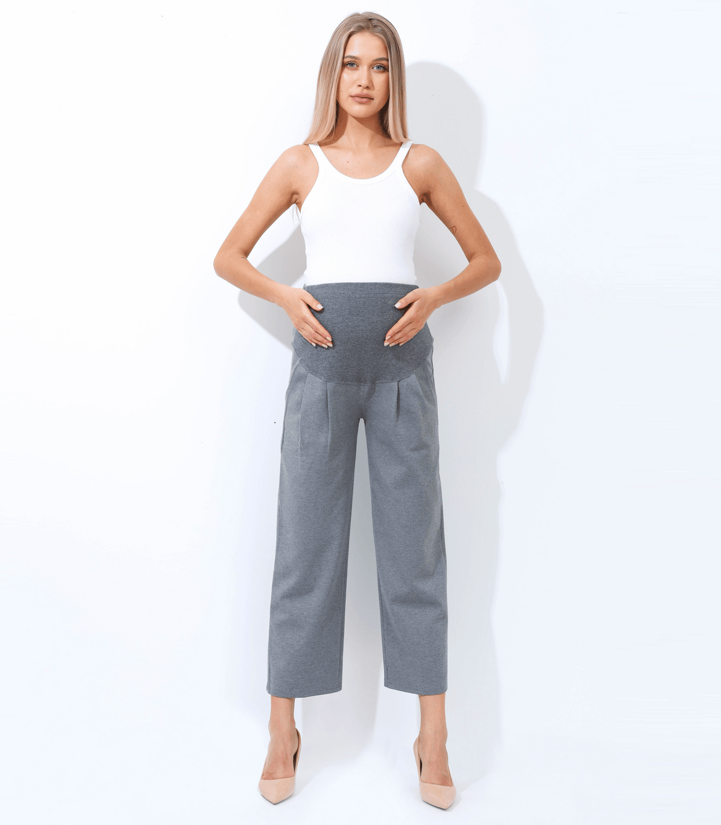 Woman wearing a white sleeveless top and gray high-waisted pants against a white background