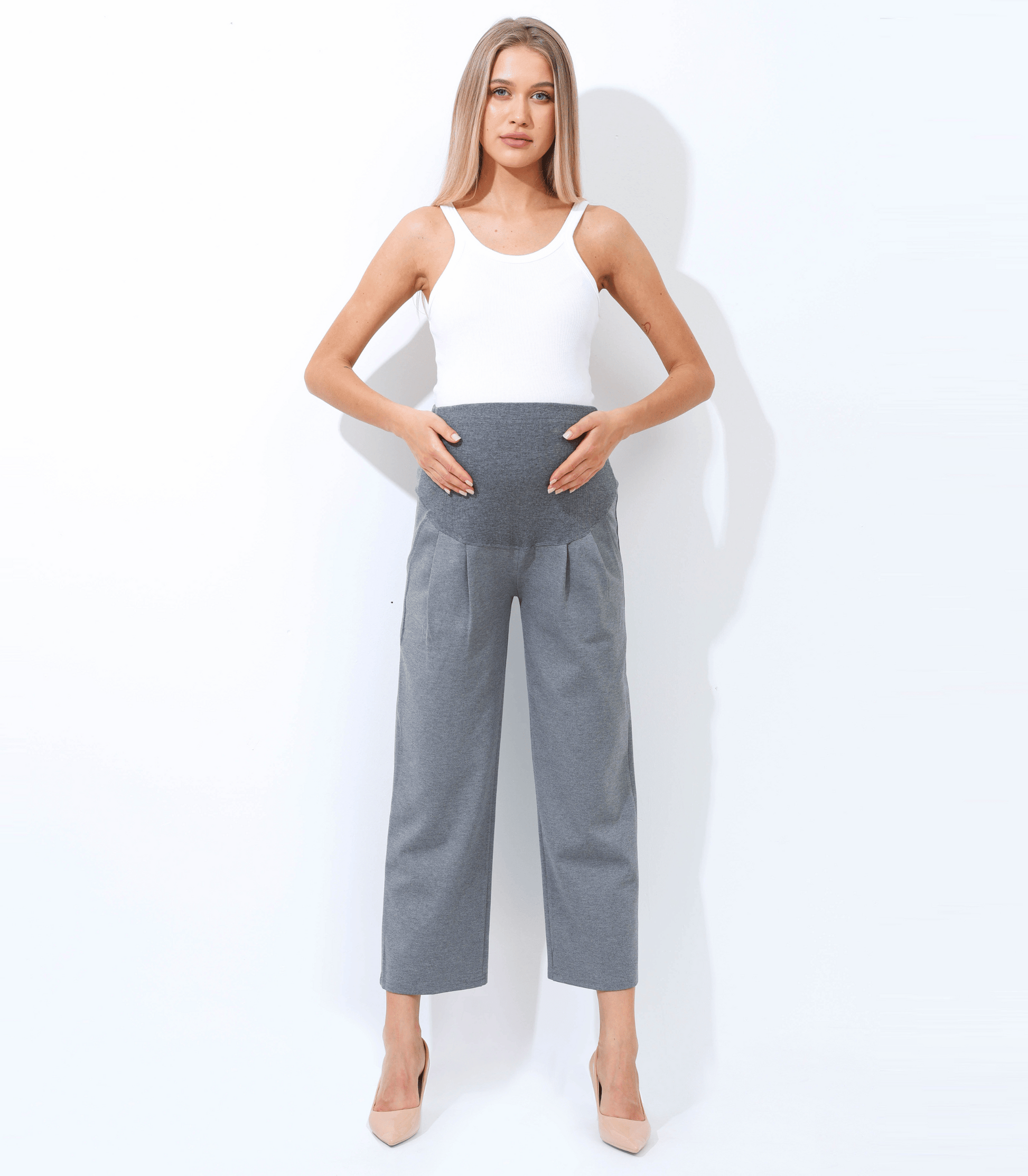 Woman wearing a white sleeveless top and gray high-waisted pants against a white background