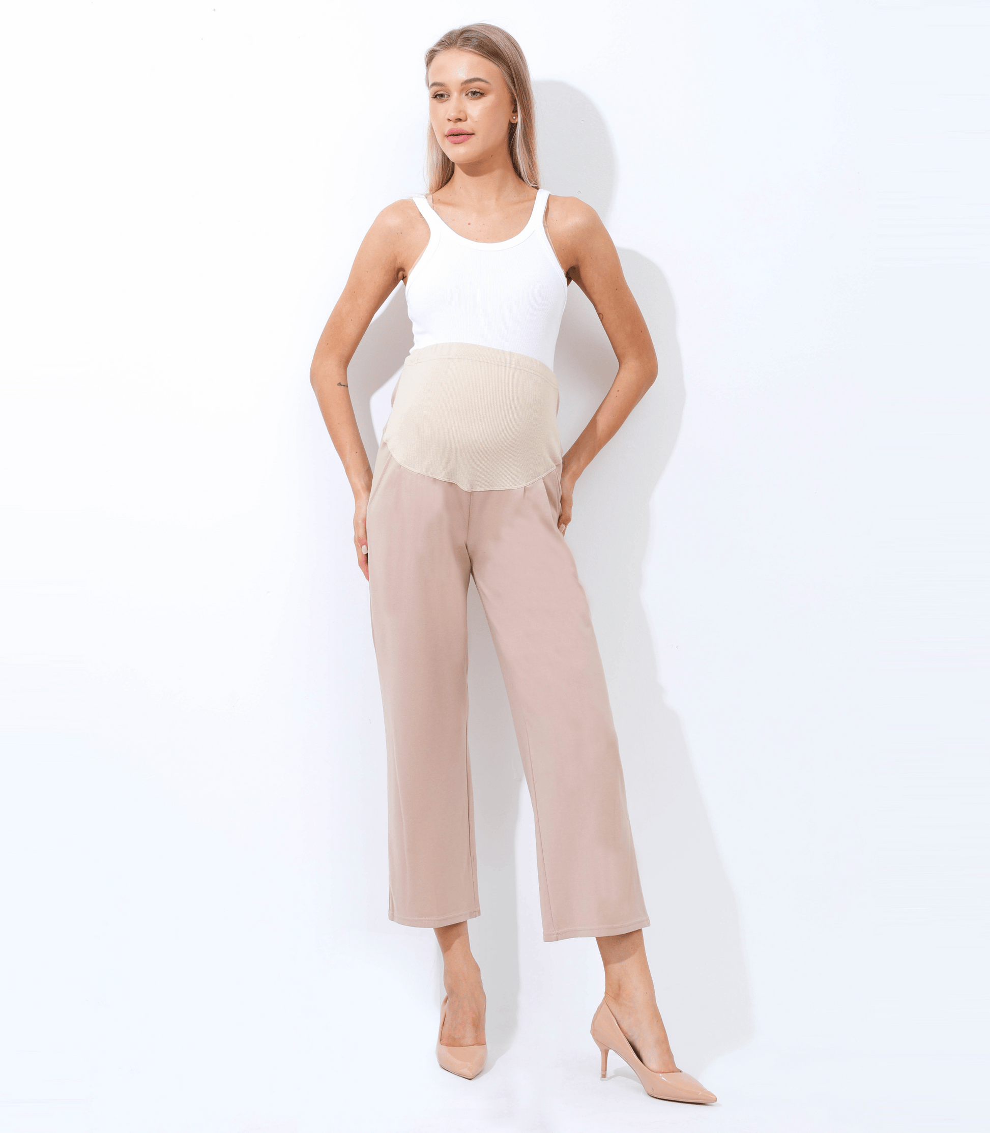 Woman wearing a white sleeveless top and beige high-waisted pants on a white background