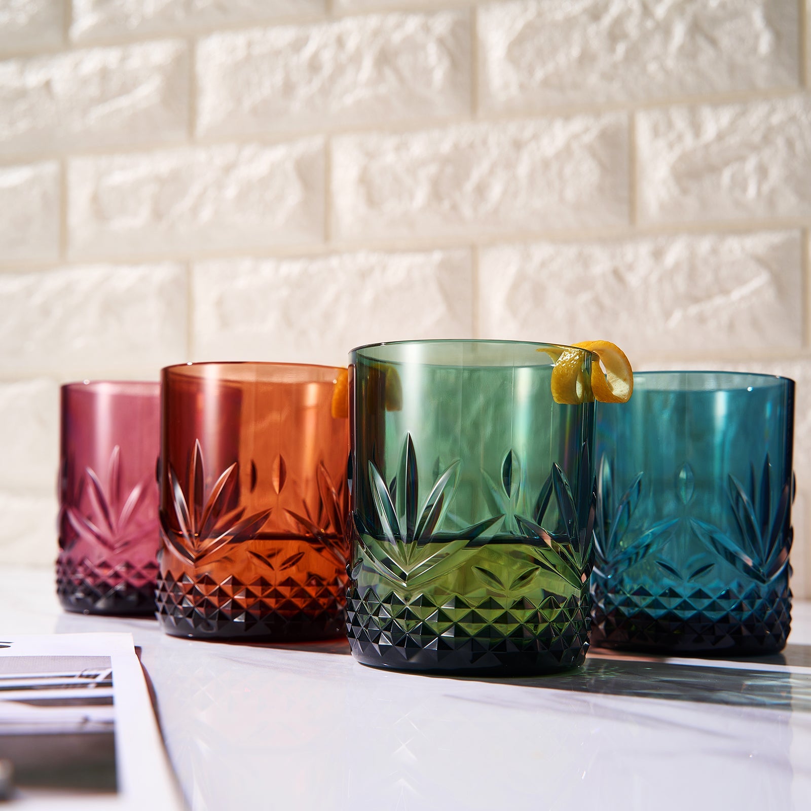 Four colorful acrylic lowball glasses with faceted base and leaf-shaped cuts