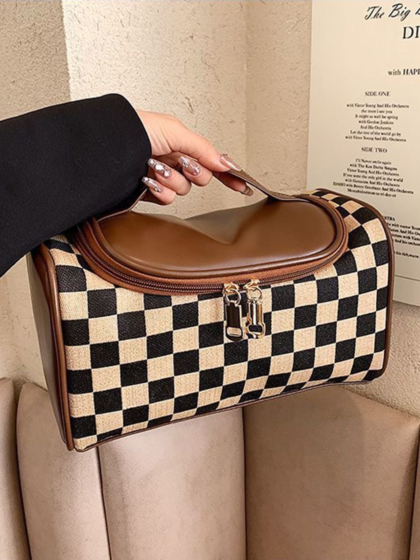 Plaid cosmetic bag with brown flap and zipper closure, resting on an upholstered seat