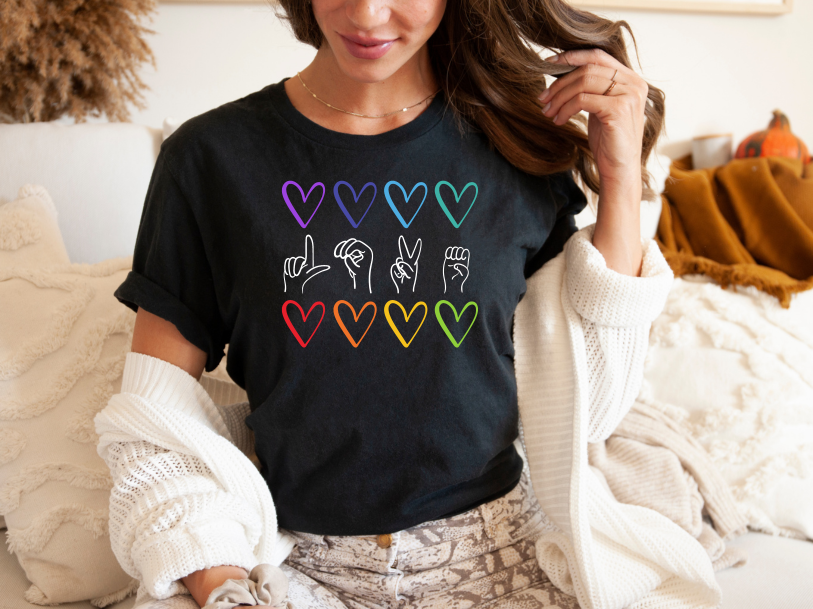 Person wearing a black t-shirt with colorful heart and hand sign designs.