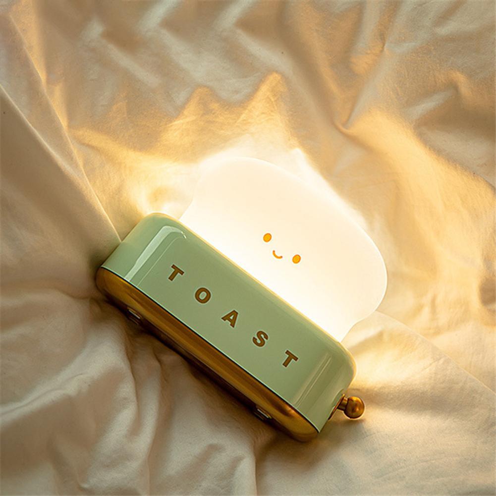 LED toaster night light on its side, green base glowing, smiling face and gold knob