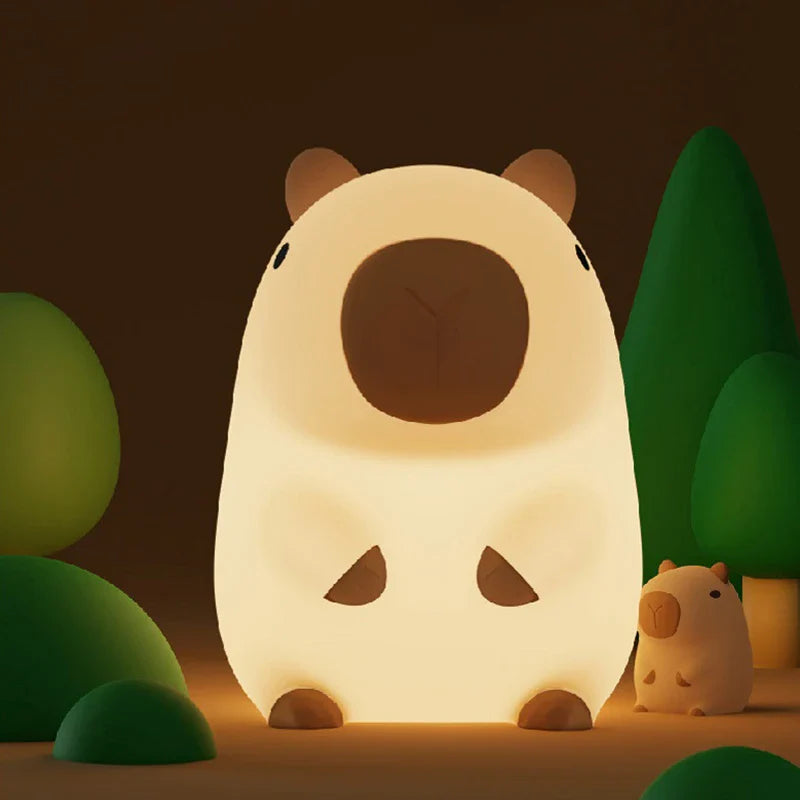 Capybara-shaped night light glowing in dark setting with small orange-knob companion