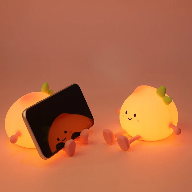 Two peach-shaped night lights glowing on floor, one beside an open book