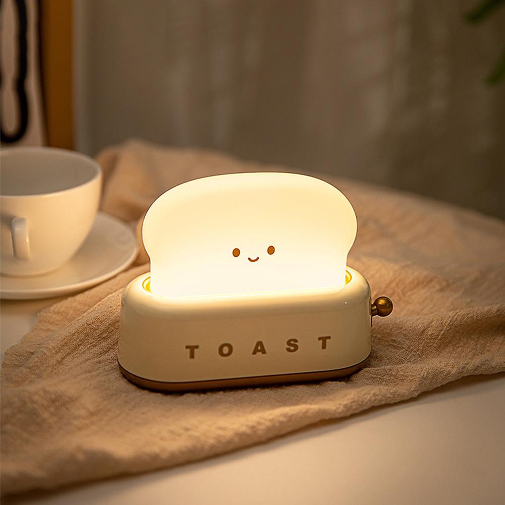 LED toaster night light glowing on beige fabric with smiling face and gold side knob