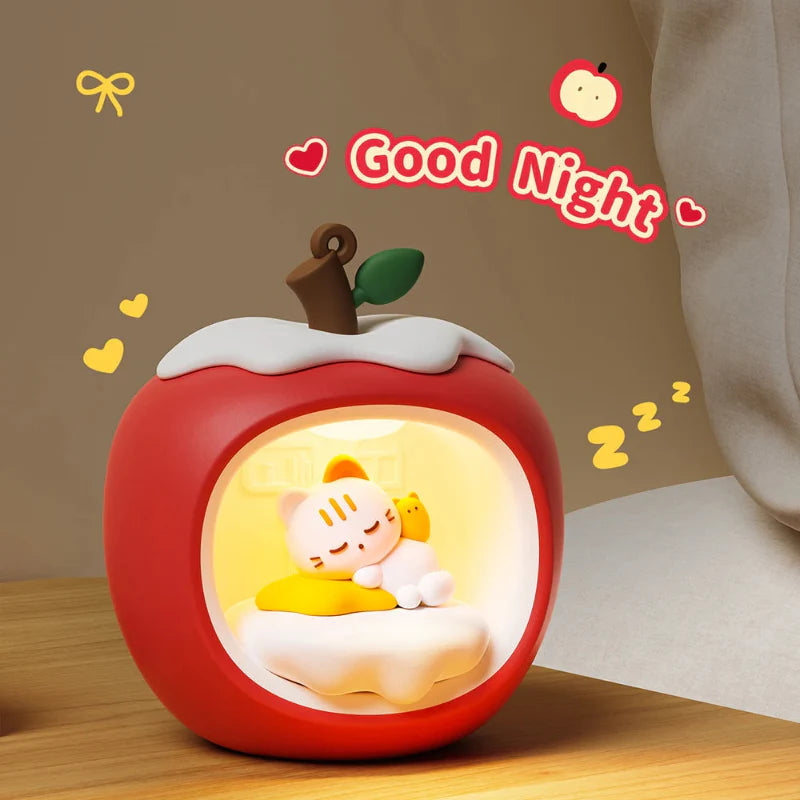 Red apple-shaped night light with sleeping cat in glowing circular panel on tabletop