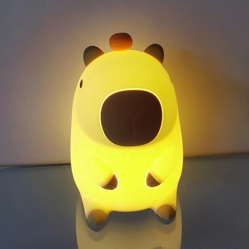 Capybara night light glowing bright yellow with orange knob on top, front view