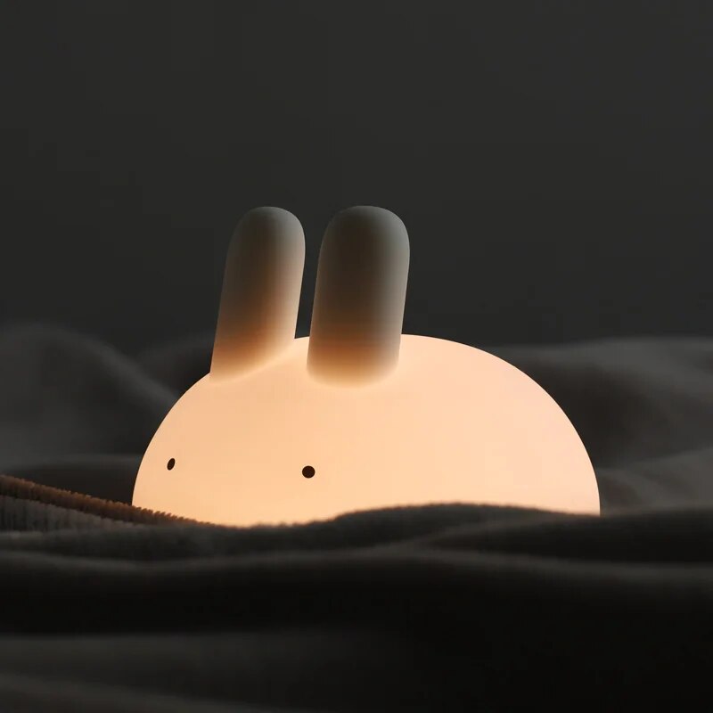 Glowing white bunny night light peeking from a blanket