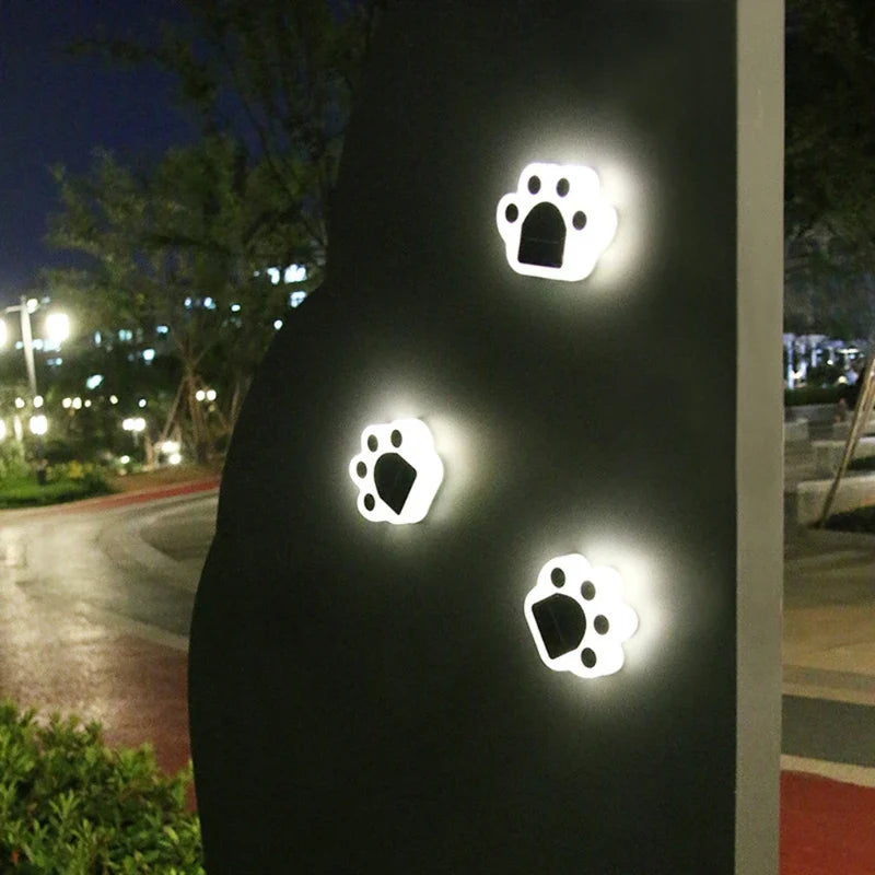 White paw-shaped solar wall or fence lights glowing at night
