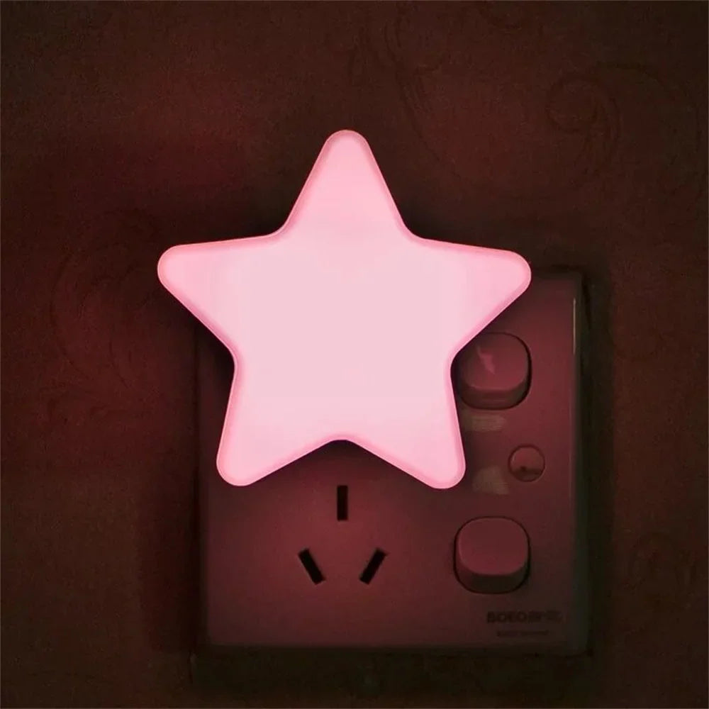 Pink star LED plug-in night light glowing on a wall outlet.