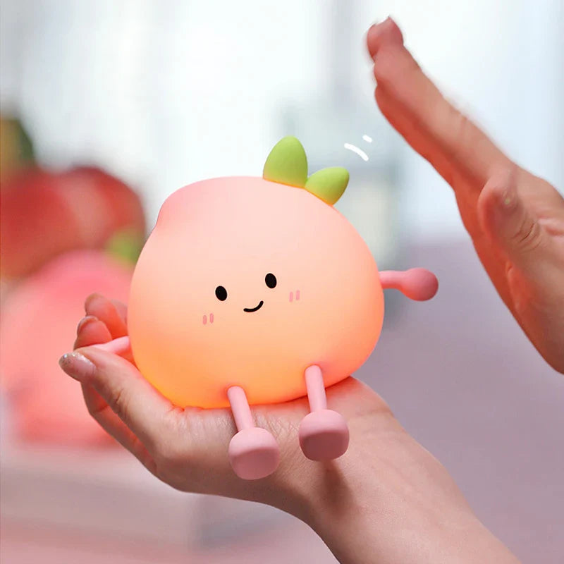 Hands holding an orange glowing peach-shaped night light with green leaf and feet