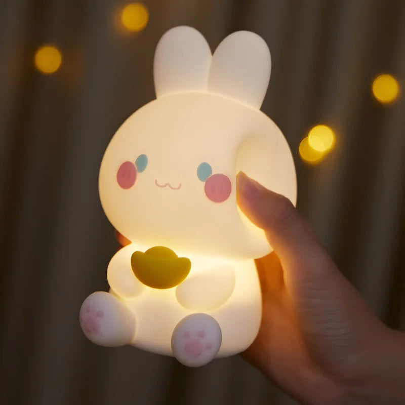 White bunny night light glowing warmly with yellow heart, viewed up close with finger