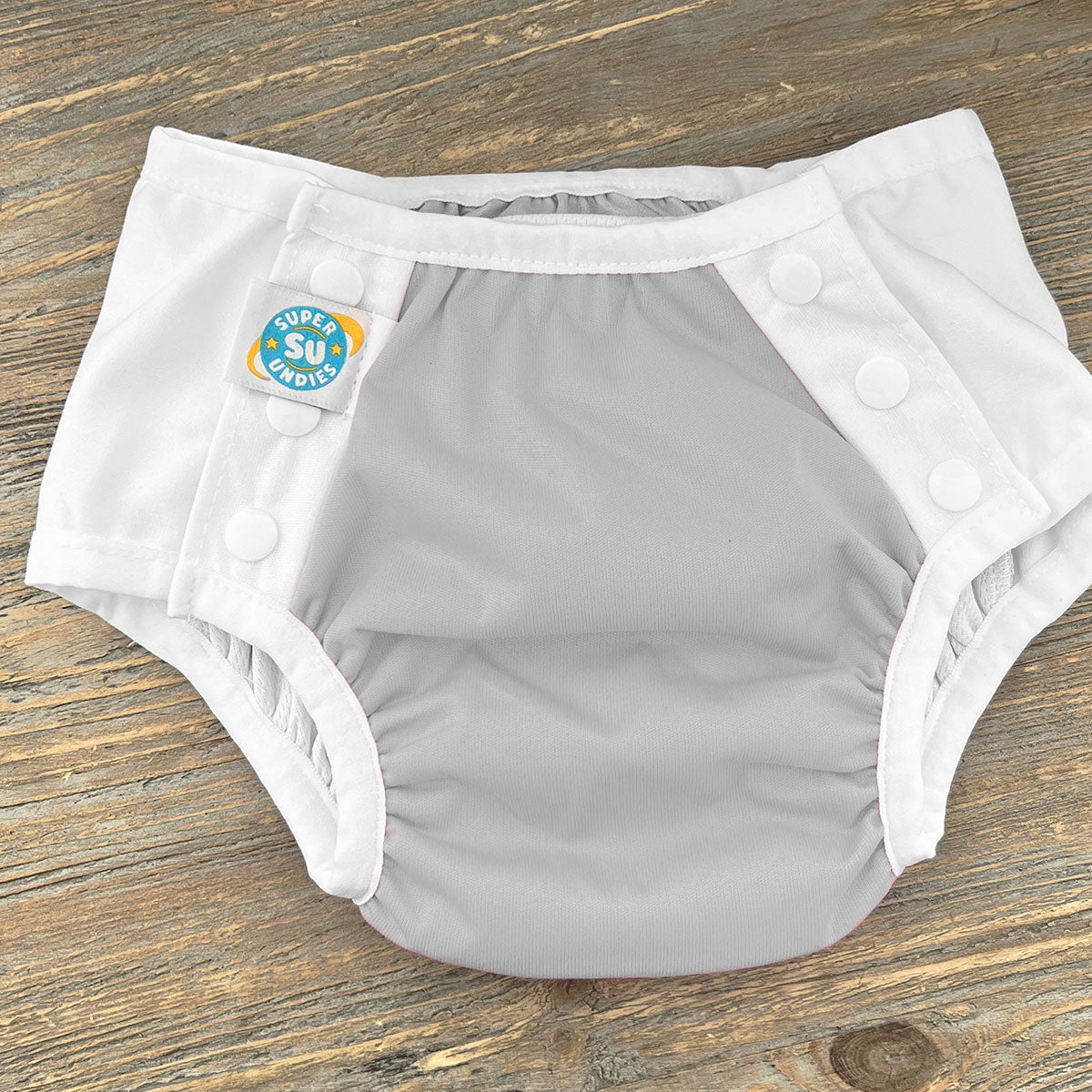 Gray diaper with white trim on a wooden surface, featuring a 'Super Su' label.