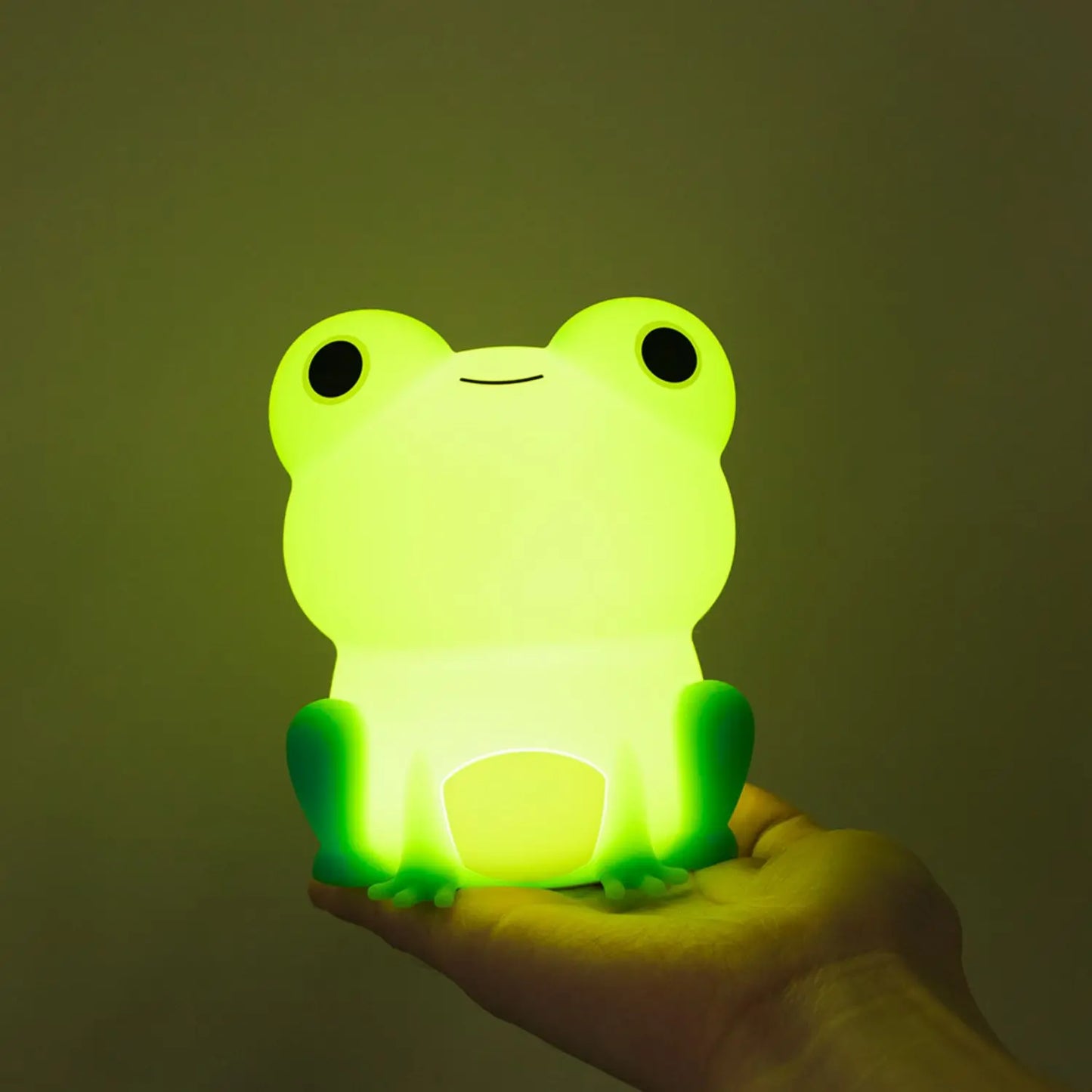 Yellow frog-shaped silicone night light, glowing and sitting on a hand.