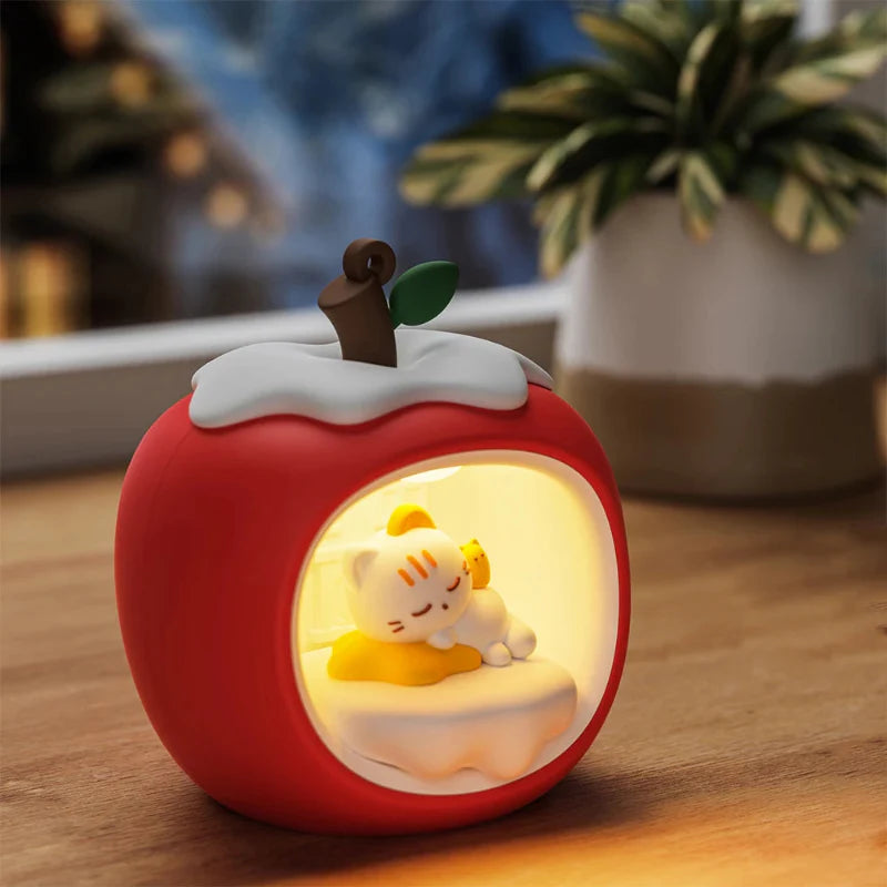 Red apple-shaped night light on wooden surface with sleeping cat glowing in front panel