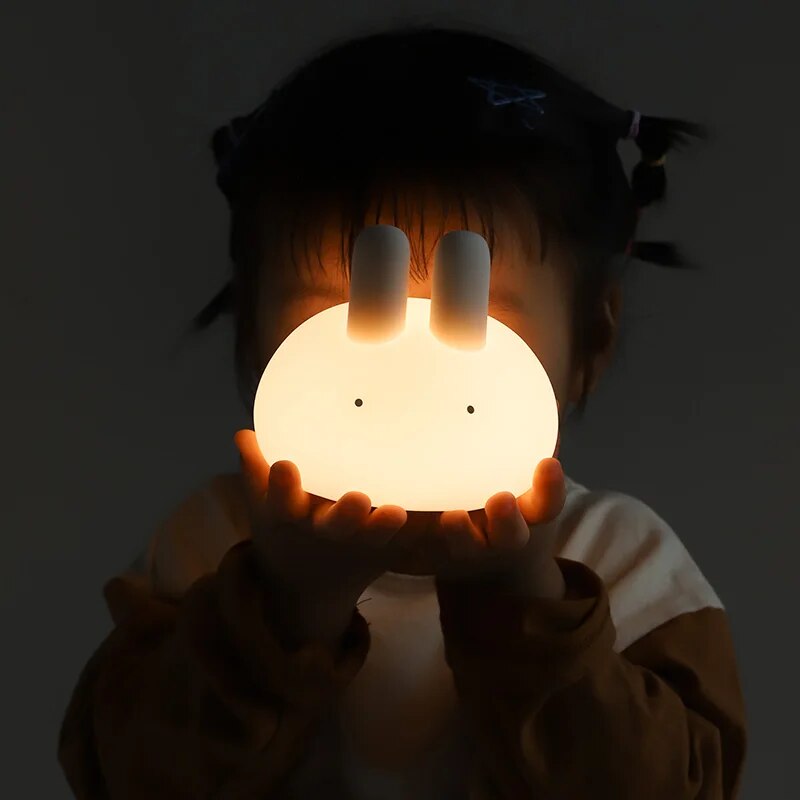 Child holding a glowing white bunny night light in dim light