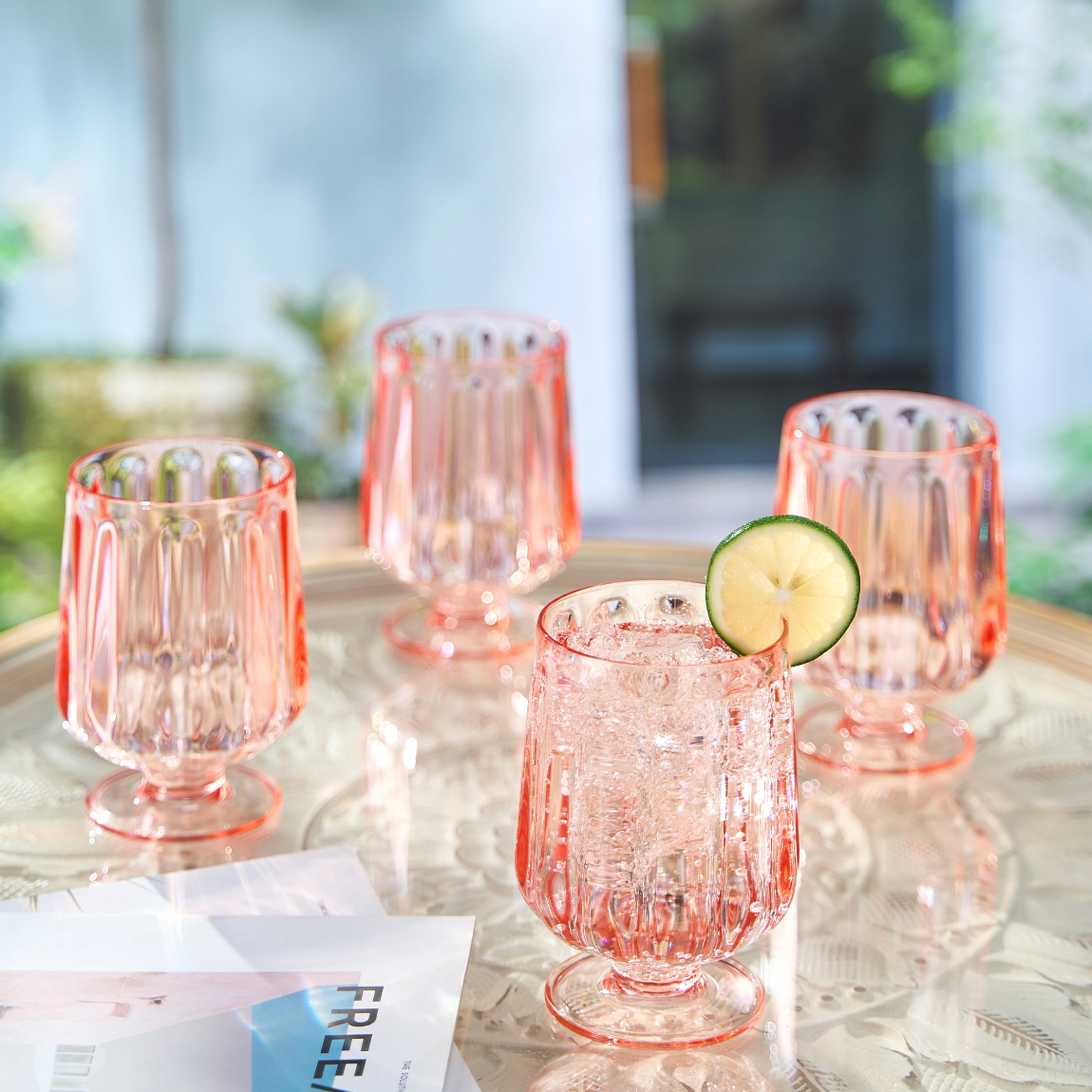 Set of four pink glasses with a lime wedge on a table outdoors