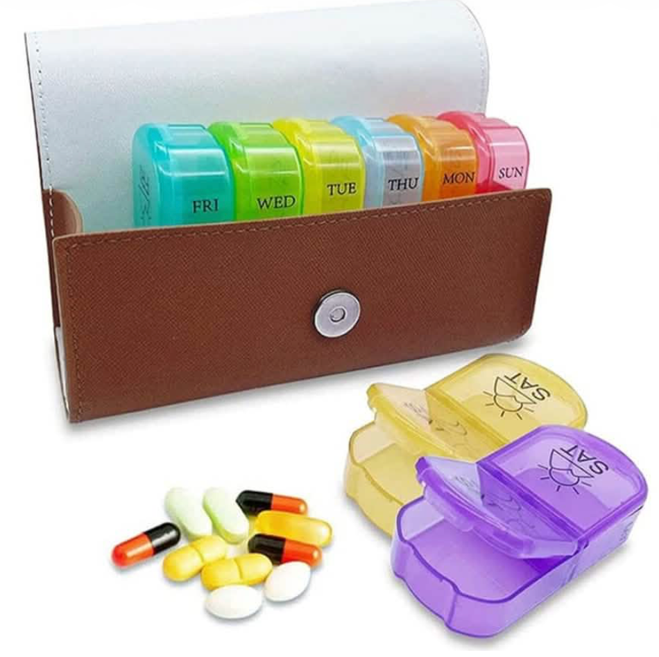 Brown pill organizer wallet with color-coded day compartments, pills, and medication boxes