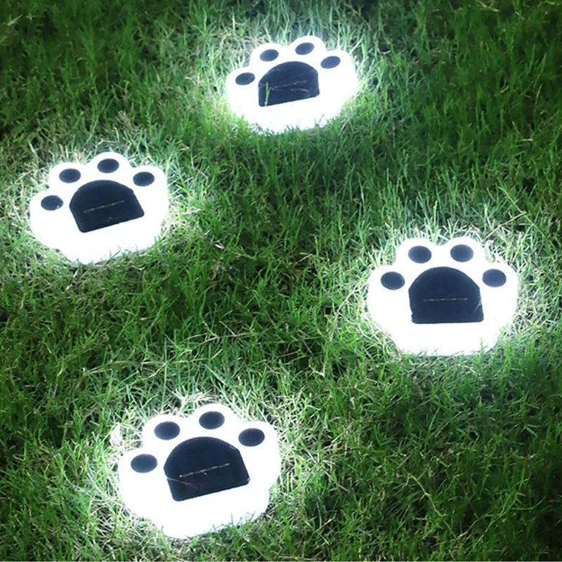 Set of white paw-shaped solar step lights glowing on green grass