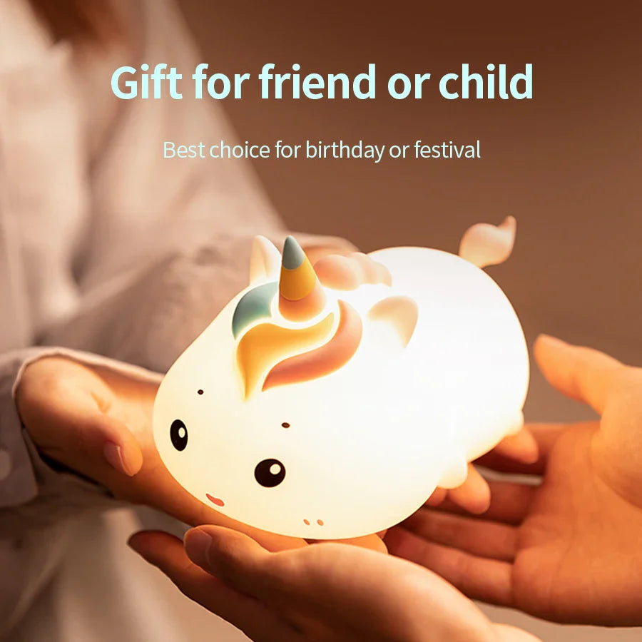 Glowing unicorn night light held by hands on a bed, horned smiling design.