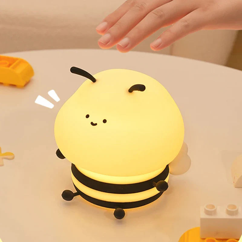 Bee night light with smiling face, yellow soft glow, and three black rings; hand above