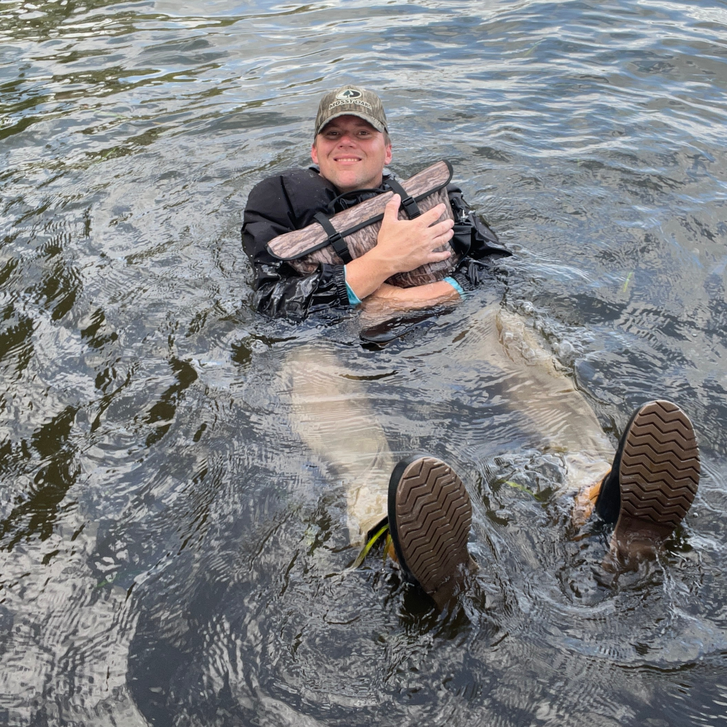 Waterproof floating cooler bag in Mossy Oak camo, floating with black straps visible