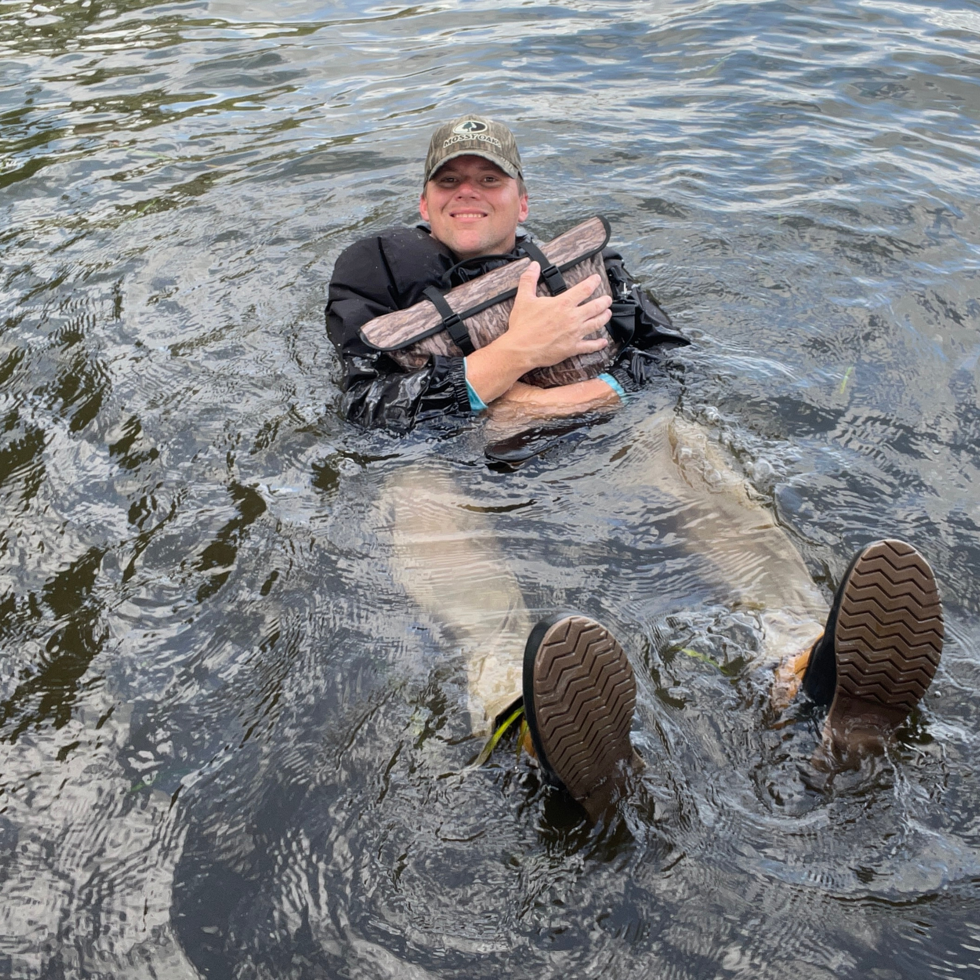 Waterproof floating cooler bag in Mossy Oak camo, floating with black straps visible
