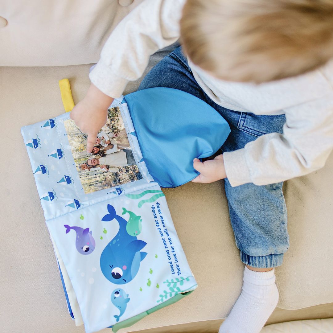 Baby holding a cloth storybook with blue cover and open photo pocket window.