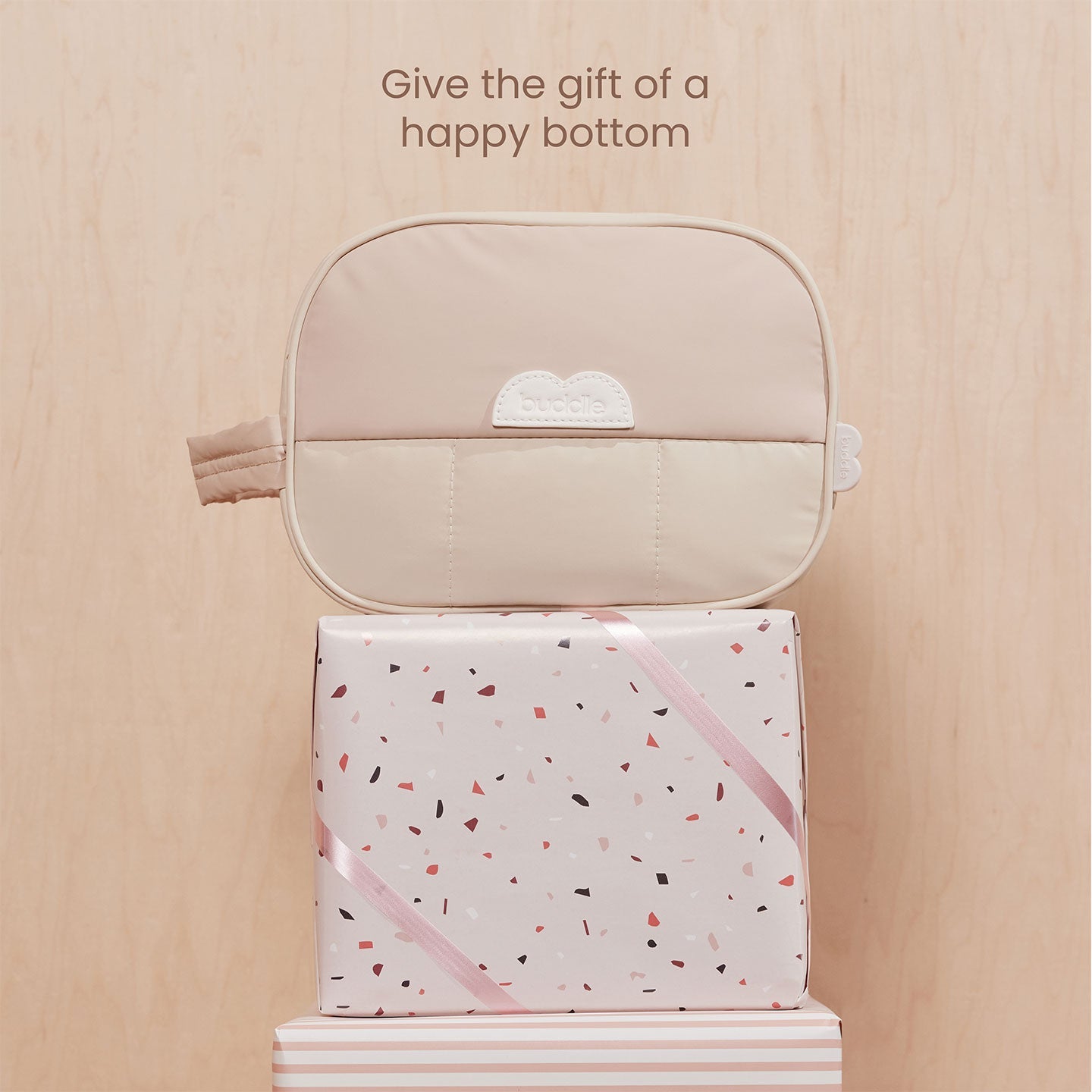 Diaper skincare kit with beige zip toiletry bag opened over patterned gift box