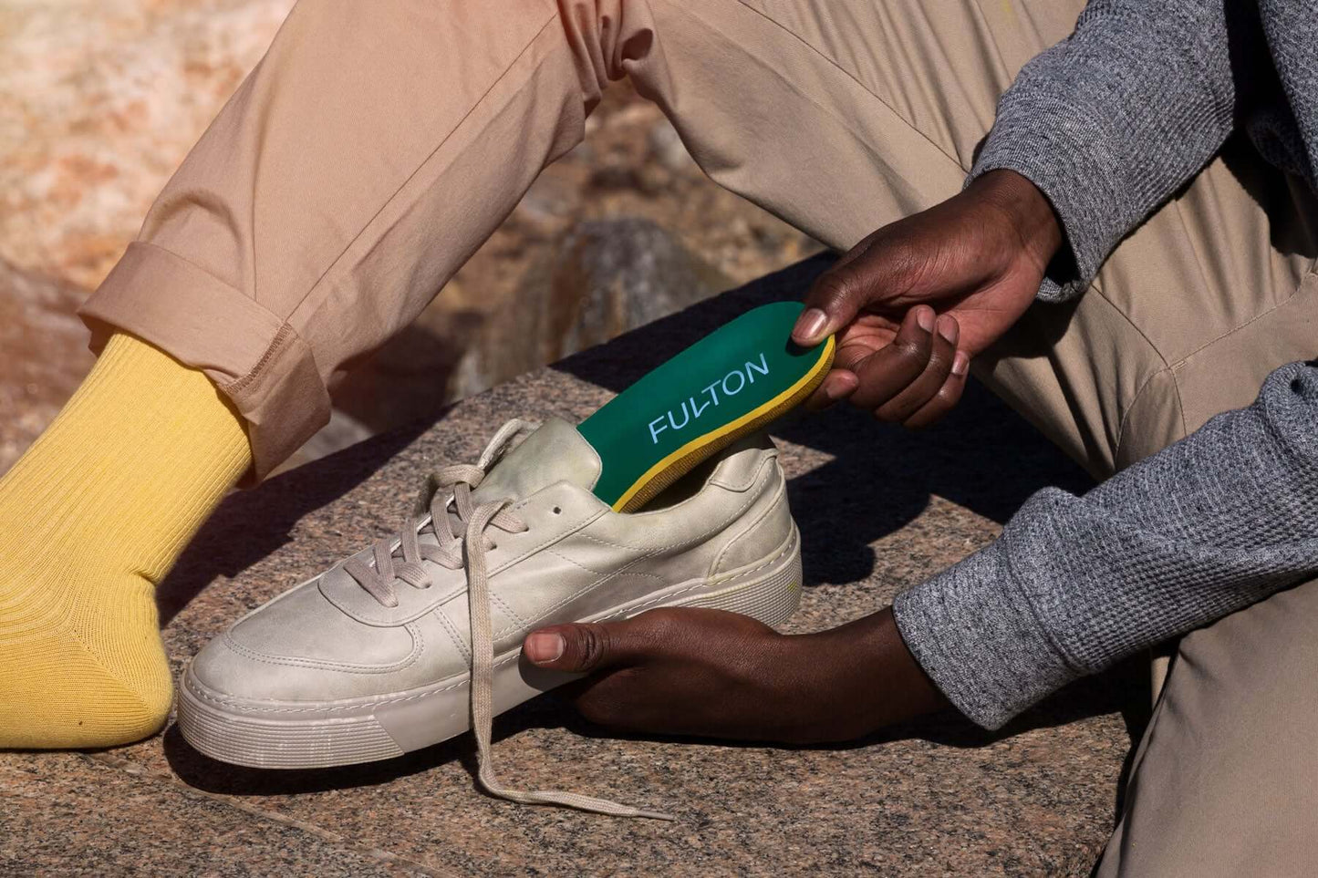 Green insole being placed into a white sneaker; hands hold the insert.