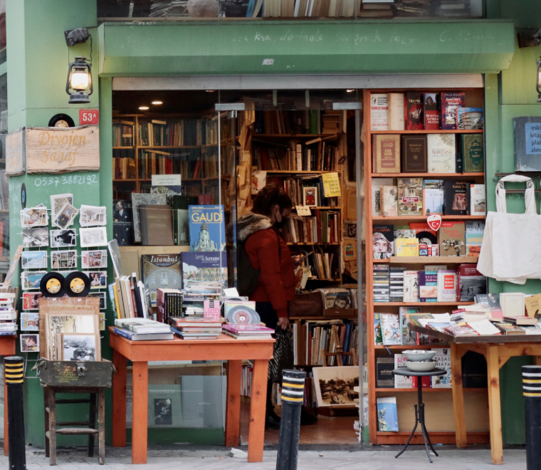 The outside of a bookshop with a green awning. Stacks onf books are surrounding the accessible entrance