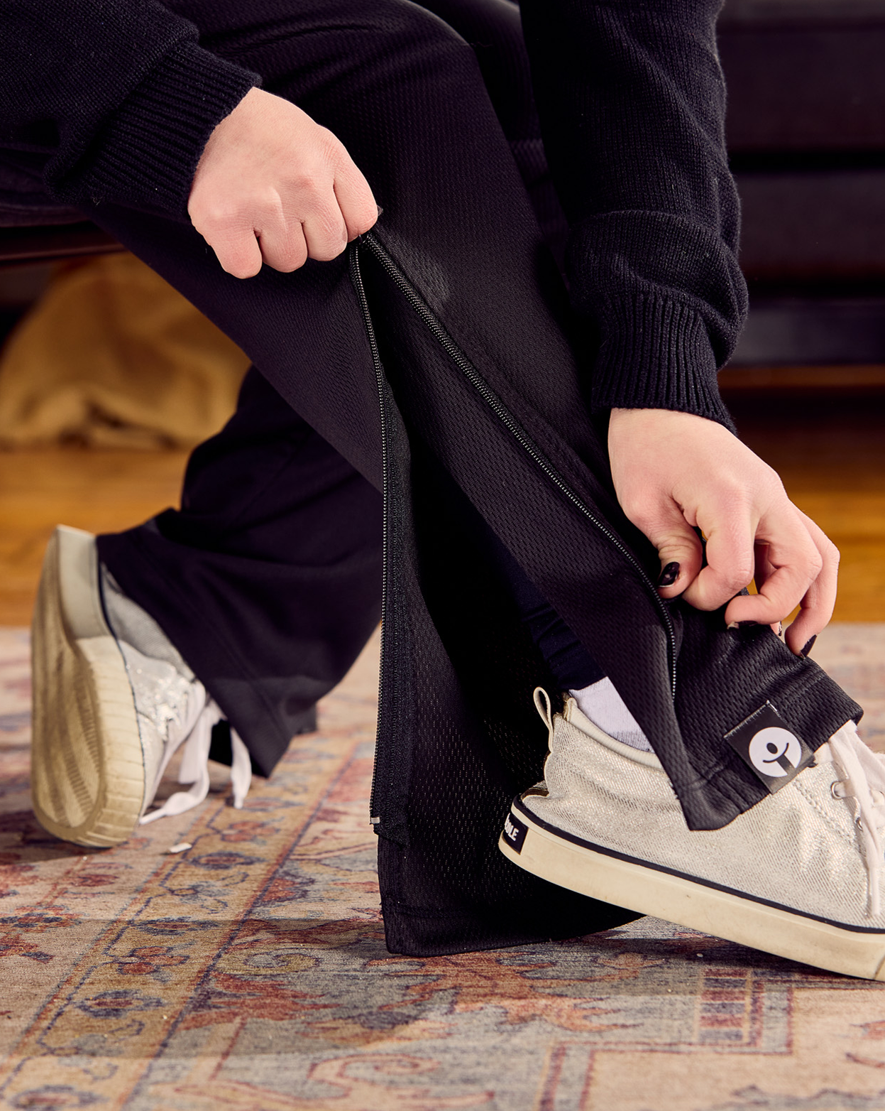 Person sitting on a patterned rug wearing black pants and white sneakers.